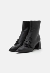 Bottines noires en cuir avec un nez pointu et un talon block. Présentent une boucle noire décorative et des coutures sur le devant.