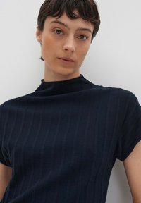 T-shirt en jersey marine à manches courtes et col haut. Le tissu a une texture lisse, avec des rayures verticales détaillées sur la surface.