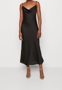 Zwarte satijnen midi-jurk met spaghetti bandjes en een draperende halslijn, met een vloeiende silhouet en een gladde textuur. Geaccentueerd met sandaalhakken met bandjes.