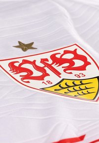 Tessuto bianco con un logo a scudo rosso e giallo, caratterizzato da motivi intricati, l'anno "1893" e una piccola stella dorata sopra l'emblema.
