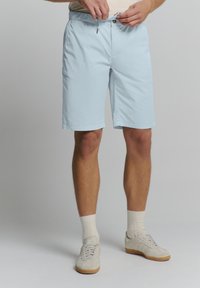 Lichtblauwe shorts met een koord in de taille, twee frontzakken en een gladde textuur. Gedirigeerd met witte sokken en crème-kleurige sneakers.
