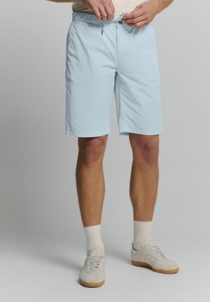 Lichtblauwe shorts met een koord in de taille, twee frontzakken en een gladde textuur. Gedirigeerd met witte sokken en crème-kleurige sneakers.