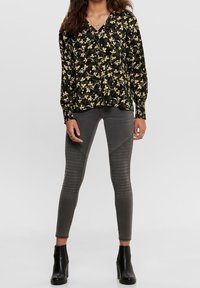 Svart blommig blus med långa ärmar, V-ringning och elastiska manschetter. Matchas med grå tajta leggings med texturerade knädetaljer. Svarta ankelsk boots.