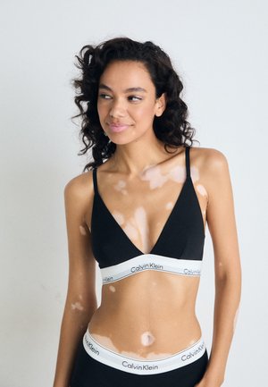 Zwarte bralette met een diepe V-hals en dunne bandjes, voorzien van een witte elastische band met het 'Calvin Klein' logo. Glad stoffen textuur.