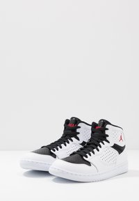 Sneaker alte con una tomaia in pelle bianca, dettagli neri, forature e un logo rosso. Suola in gomma con finitura testurizzata.