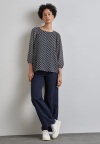 Haut transparent à motifs géométriques navy avec des manches trois-quarts, associé à un pantalon navy décontracté et des baskets blanches. Textures lisses tout au long.