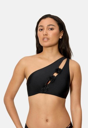 Mujer con un bikini negro de un solo hombro con tres flores de tela decorativas a lo largo de un corte diagonal.