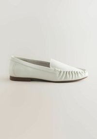 Šviesiai žalias plokščias batai su minkštu odiniu viršumi, apvaliu noselė ir raukšlėta detalizacija palei siūlę. Žemas rudas kulnas stabilumui.