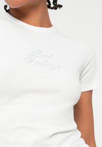 T-shirt bianca realizzata in tessuto morbido, con maniche corte e collo rotondo. Testo "Mixed Feelings" in strass argentati sul davanti.