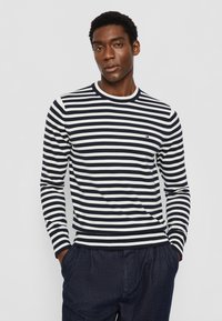 Camisa de mangas longas às riscas azul-marinho e brancas, com um decote redondo e punhos canelados. Apresenta um pequeno logotipo no peito. Tecido de malha suave.