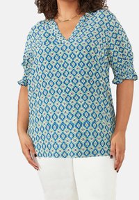 Blusa blu a motivo con scollatura a V, maniche corte e vestibilità rilassata. Presenta un design geometrico in tonalità di blu, verde e bianco.
