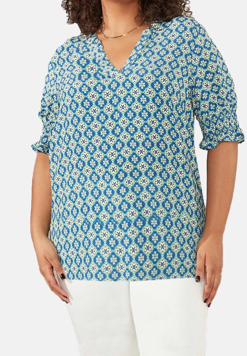 Blusa blu a motivo con scollatura a V, maniche corte e vestibilità rilassata. Presenta un design geometrico in tonalità di blu, verde e bianco.
