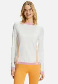 Maglione bianco a maglia con strisce laterali rosa e arancioni, colletto a coste rosa e maniche lunghe. Abbinato a leggings arancioni.