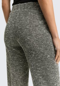 Gestructureerde broek met hondentandpatroon in zwart-wit; voorzien van een aansluitende taille en een wijd uitlopende pijp, met nadruk op de diepte en details van de stof.