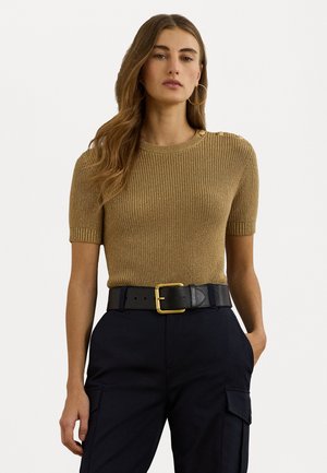 Pull en maille côtelée à manches courtes de couleur or métallique, avec des détails de boutons aux épaules. Associé à une ceinture noire et un pantalon sombre.