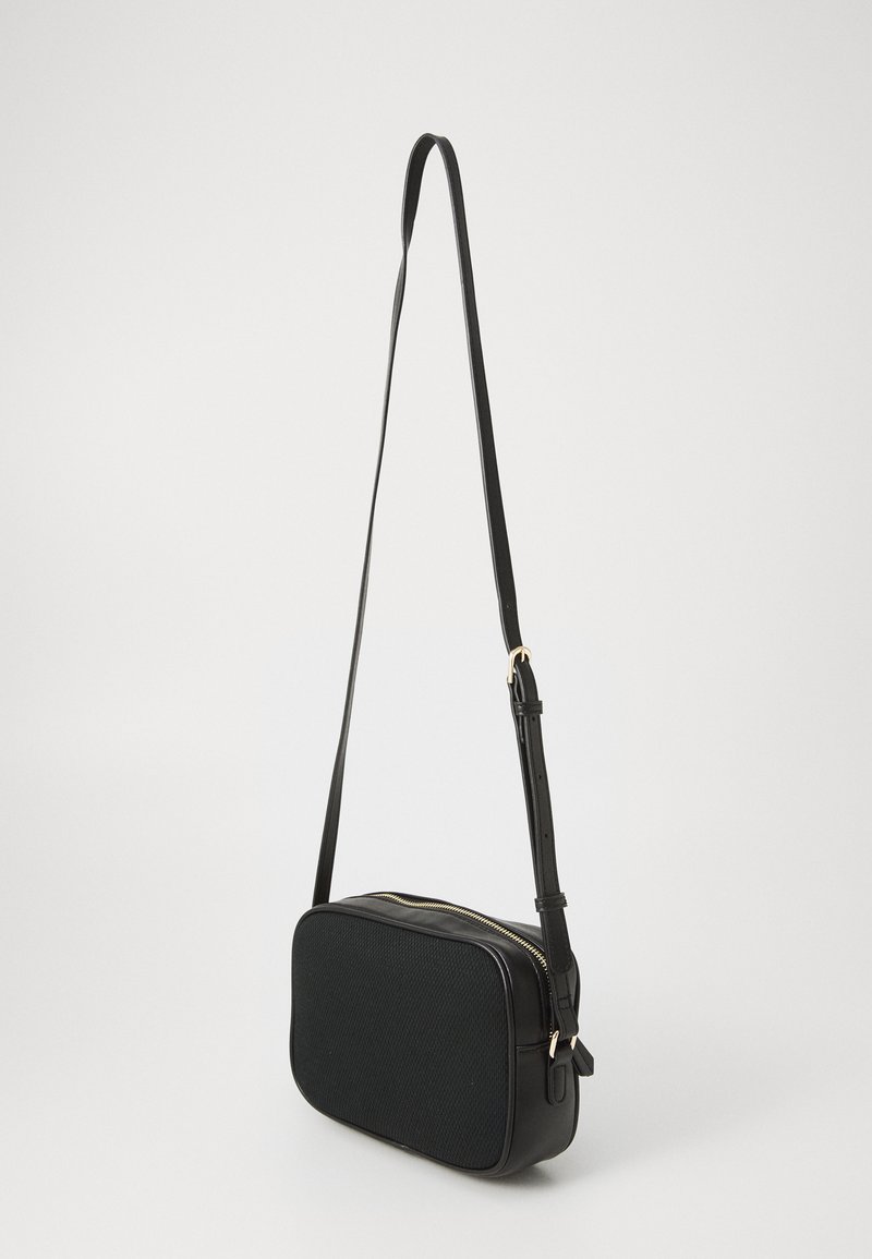 Sac à bandoulière noir de forme rectangulaire, devant en tissu texturé, dos en cuir lisse, bandoulière ajustable et détails de fermeture éclair dorés.