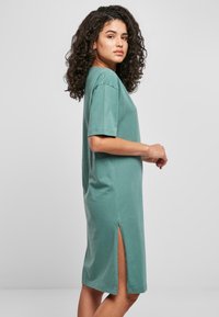 Tijlgroene katoenen jurk met korte mouwen, een rechte silhouet en zijsplitsingen. Gladde textuur en casual ontwerp, geschikt voor diverse gelegenheden.