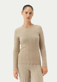 Beige ribbstickad tröja med långa ärmar, rund halsringning och figurnära silhuett, tillverkad av mjukt material med vertikala ränder.