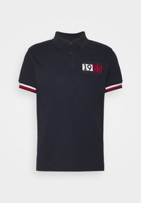 Marineblauwe polo shirt van katoen met een twee knopen sluiting. Beschikt over contrasterende rode en witte strepen op de mouwen en een logo ontwerp met '1985'.
