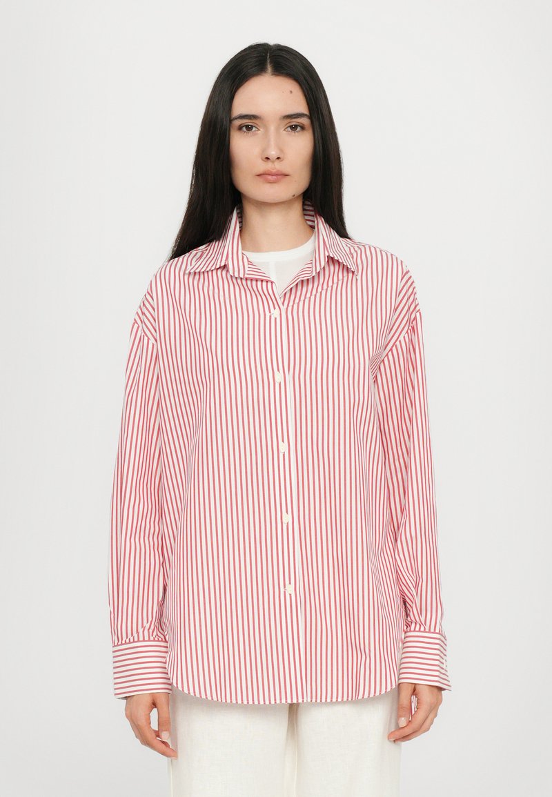 Rdeča in bela prugasta srajca z dolgimi rokavi, ovratnikom in belimi gumbi. Tkanina se zdi gladka s rahlo sijajno teksturo.