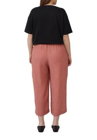 Haut noir à manches courtes avec un col rond, associé à un pantalon court texturé de couleur rose pâle. Des chaussures noires perforées à enfiler complètent l'ensemble.