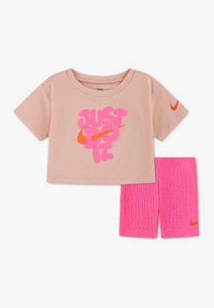 Lyserød T-shirt med korte ærmer med teksten "JUST DO IT." i pink og orange, kombineret med lyserøde, strukturerede shorts, begge med orange Nike-logoer.