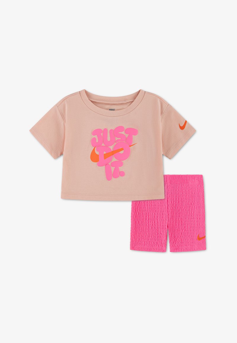 T-shirt rose clair à manches courtes avec l'inscription « JUST DO IT. » en rose et orange, associée à un short texturé rose vif, tous deux ornés de logos Nike orange.