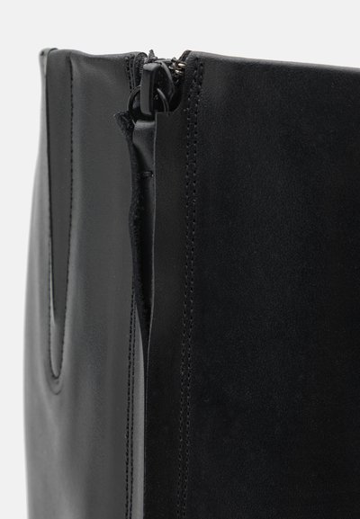 Svart läderväska med en slät textur, vertikal design och dragkedjestängning. Sömnadsdetaljer längs kanterna ger strukturen.
