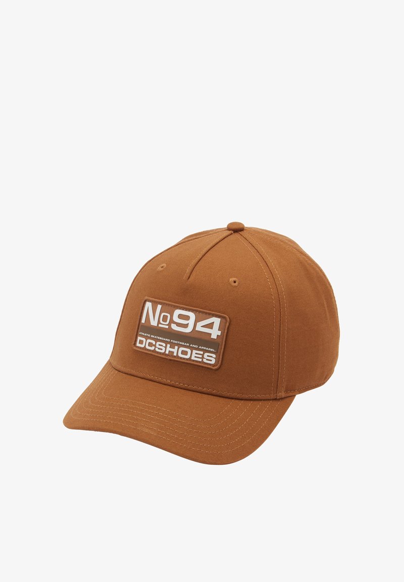Gorra marrón de algodón, con un parche frontal que muestra "No94 DCSHOES" en blanco y gris sobre un fondo rectangular.