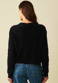 Marinblå kabelstickad tröja med en kortad design och ribbad rundad halsringning. Har texturerade mönster på ärmarna och en figursydd nederkant.