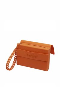 Borsa rettangolare arancione realizzata in materiale di gomma testurizzata, con chiusura a zip e tracolla a catena. Logo Havaianas impresso sulla parte anteriore.