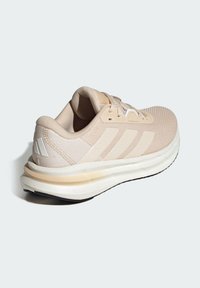 Baskets de sport beiges avec une tige en mesh texturé, trois bandes blanches, un col rembourré et une semelle rembourrée bicolore.