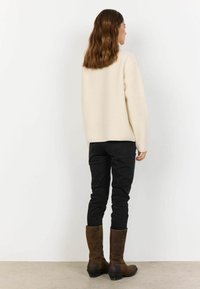 Cremefarvet fluffy sweater, sorte slim-fit jeans og brune læderstøvler til knæene; simpelt design med minimale detaljer.