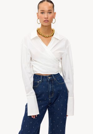 Blouse blanche à enrouler avec de longues manches volumineuses et un décolleté en V profond. Assortie à un jean en denim bleu taille haute avec de petites touches.