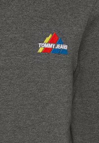 Šedá mikina s texturou látky. Vyšitá logo s červenými, žlutými a modrými trojúhelníky a nápisem "TOMMY JEANS" na hrudi.