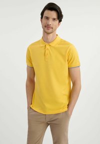 Żółta koszulka polo z klasycznym kołnierzykiem, pięcioma guzikami i szarymi akcentami na rękawach. Gładki materiał z małym logo na piersi.