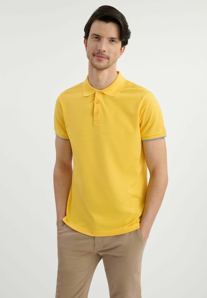 Żółta koszulka polo z klasycznym kołnierzykiem, pięcioma guzikami i szarymi akcentami na rękawach. Gładki materiał z małym logo na piersi.