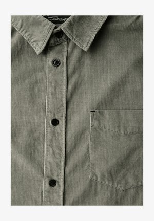 Grünes Cordhemd mit spitzem Kragen, fünf schwarzen Knöpfen und einer linken Brusttasche. Der Stoff ist gerippt mit einer weichen Oberfläche.