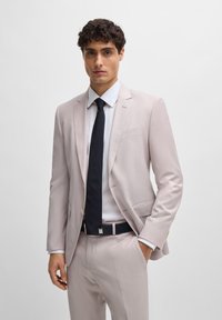 Blazer rosa claro com calças a condizer, camisa branca e gravata escura. Apresenta um design ajustado, textura suave e detalhes em costura subtil.