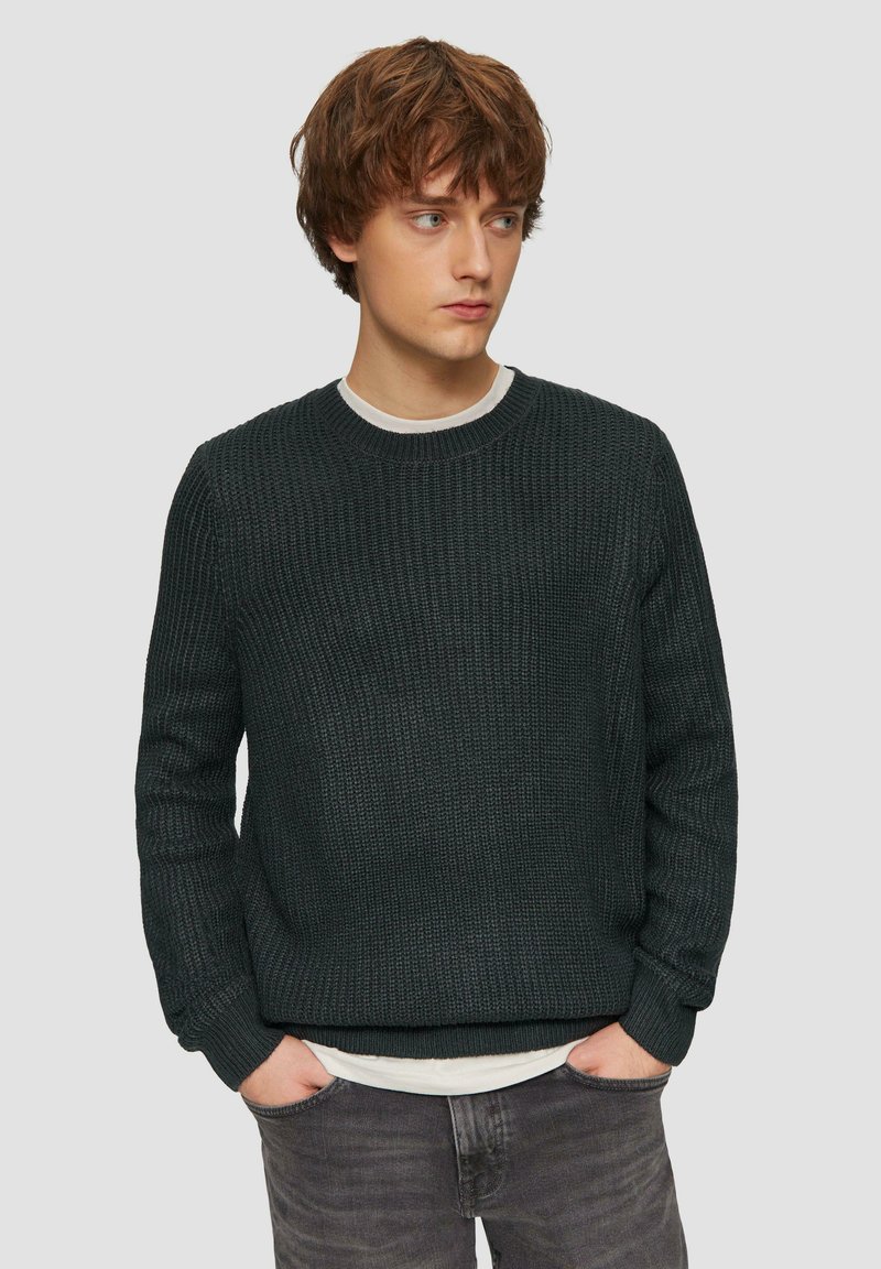 Dunkelgrüner Strickpullover mit strukturiertem Muster, Rundhalsausschnitt, gerippten Bündchen und Saum, über einem hellen Hemd getragen.