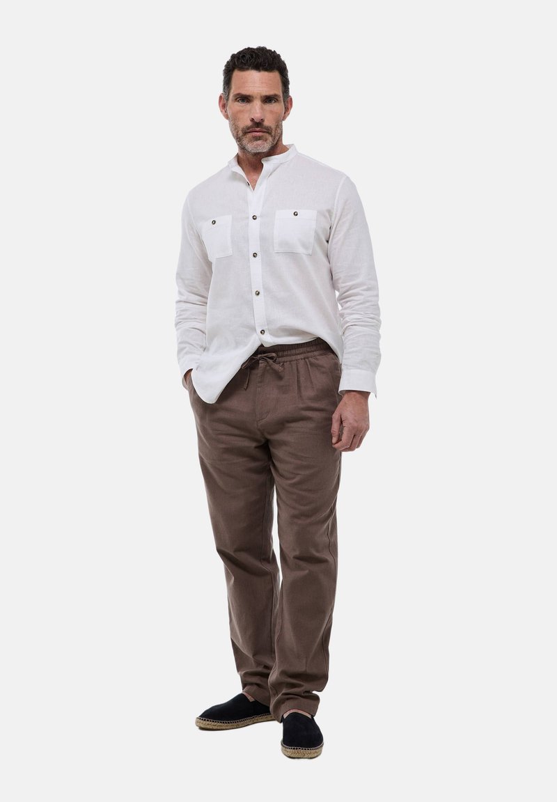 Chemise blanche à manches longues avec deux poches poitrine, pantalon en cordon de serrage marron et espadrilles noires ; dotée de fermetures à bouton et d'une coupe décontractée.