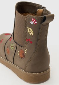 Botte basse marron avec des côtés élastiques, présentant des motifs colorés brodés de feuilles, de champignons et d'un oiseau sur le côté extérieur.