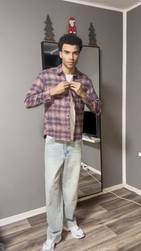 Flanellhemd in rosa und lila kariert, leicht zugeknöpft, kombiniert mit hellblauen Jeans und weißen Turnschuhen. Steht in einem Zimmer mit Spiegel.