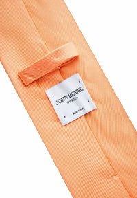 Orange randig tyg med en slät textur, med en sydd etikett som läser "John Henric, Sverige, Tillverkad i Italien."