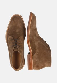 Brązowe zamszowe eleganckie buty z gładkim wykończeniem, skórzanymi sznurowadłami, okrągłym noskiem i drewnianym obcasem. Szwy wzdłuż podeszwy.