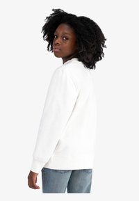 Witte sweatshirt met lange mouwen en geribbelde manchetten, gecombineerd met blauwe spijkerbroek. Heeft een ronde halslijn en een zachte textuur.