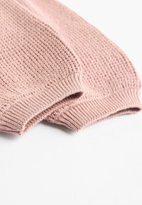Primer plano de los puños acanalados de un suave suéter de punto rosa, mostrando la textura detallada de las costuras sobre un fondo blanco.