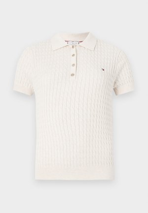 Polo beige clair en maille avec manches courtes, motif diamant texturé, patte de boutonnage à trois boutons et petit logo brodé sur la poitrine.