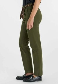 Olijfgroene broek met een rechte snit, voorzien van een riem van luipaardprint die om de taille is geknoopt. Draagt zwarte instappers.