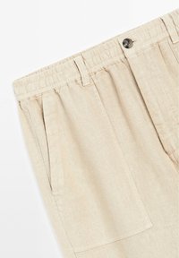 Pantalons en lin beige avec une taille élastique, dotés d'une fermeture à bouton et de poches latérales, en tissu texturé et à coupe décontractée.